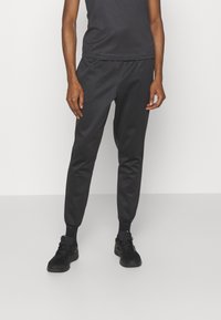 Black jogger pants made of a smooth, lightweight material with elastic cuffs. Paired with a fitted black tank top and black sneakers.