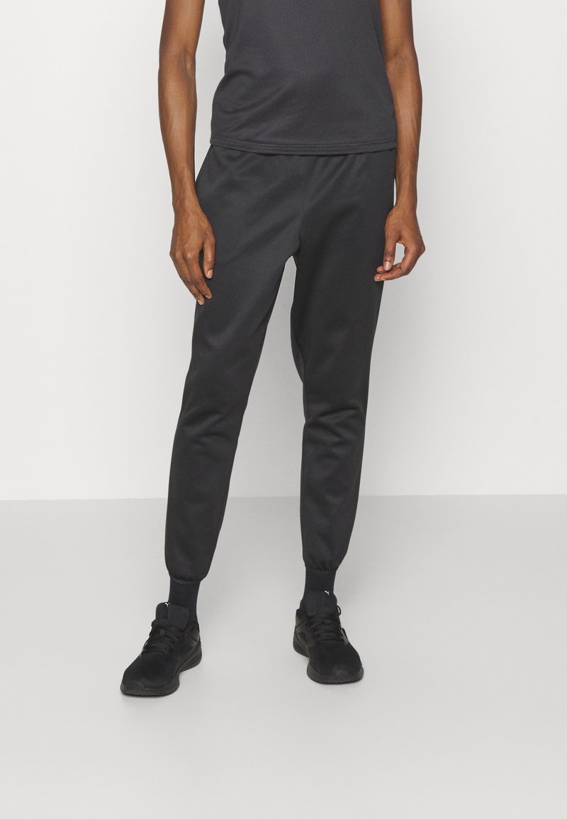 Black jogger pants made of a smooth, lightweight material with elastic cuffs. Paired with a fitted black tank top and black sneakers.
