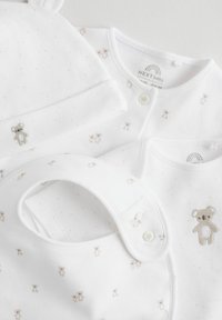 White baby clothing set including a hat, bodysuit, and bib. Features include soft fabric, teddy bear embroidery, and small dot patterns.