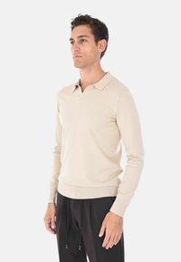 Maglione polo beige a maniche lunghe con scollatura a V, polsini e orlo a coste, realizzato in un tessuto liscio e morbido. Design leggero e aderente.