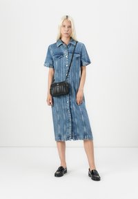 Abito camicia in denim di un blu chiaro, con maniche corte, chiusura frontale con bottoni e strisce verticali. Abbinato a una piccola borsa a tracolla nera e mocassini.