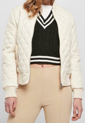 Personne portant un pull court noir et blanc à col en V, un pantalon beige taille haute et une veste matelassée crème avec des poignets côtelés.
