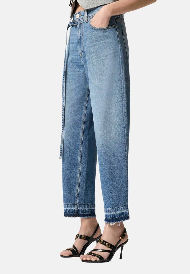 Persona che indossa jeans corti azzurri con orli sfrangiati e sandali neri con tacco alto e cinturini, dettagli con fibbia dorata.