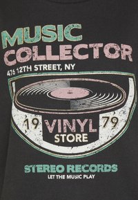 Svart t-shirt med en retro vinylskivgrafik. Texten i rosa och grönt säger "MUSIKSAMLARE," med "VINYLBUTIK" och platsinformation nedanför.