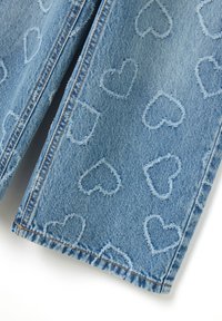 Versleten blauwe denimstof met reliëf hartpatronen in een lichtere tint, met contrasterende stiksels langs de naden.