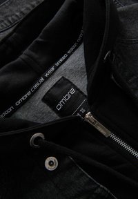 Felpa nera con chiusura a zip, texture morbida e fodera interna grigia. Presenta un'etichetta con il marchio "ombre casual wear limited edition".