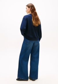 Μπλε σκούρο φούτερ με άνετη εφαρμογή, συνδυασμένο με φαρδιά τζιν παντελόνια μπλε χρώματος, με κλασικό σχέδιο πέντε τσεπών και διακριτικό ξεβάμμα.