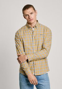 Geel en grijs geruit overhemd met knopen, lange mouwen, kraag, lichtgewicht stof, voorzak met merklLogo, gecombineerd met lichtblauwe jeans.