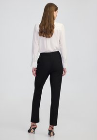 Bílá halenka s dlouhými rukávy, kombinovaná s černými slim-fit kalhotami a černými sandály na podpatku. Jednoduchý design, hladká látka a dobře padnoucí střih.