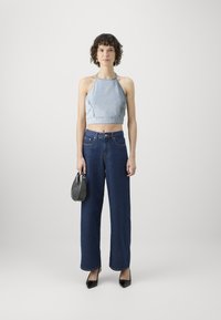 Top corto in denim celeste con scollo a halter abbinato a jeans a vita alta blu scuro a gamba larga, tacchi neri a punta e una piccola borsa nera.