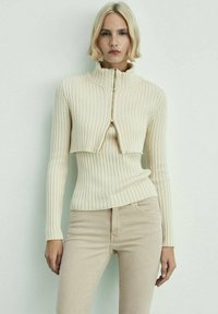 Fitted, ribbet sweater i off-white med høj krave og guld lynlås. Afkortet design med lange ærmer og en struktureret strik.