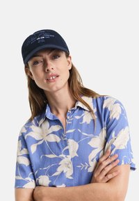 Marineblå baseballcaps med brodert teksten "New Haven", kombinert med en blå shortsleeve skjorte med blomstermønster som har hvite blomsterdesignet.