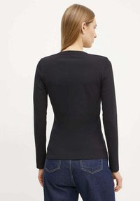 Camiseta negra de manga larga hecha de tejido elástico, con un diseño ajustado y un cuello redondo. La vista trasera muestra una textura suave.