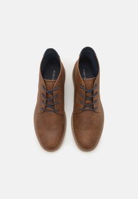 Chaussures en cuir marron avec une texture lisse, bout rond et lacets bleu marine. Elles présentent une semelle cousue et un logo sur la languette.