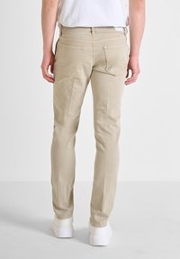 Jeans de algodón beige con un corte ajustado, que cuentan con dos bolsillos traseros, costuras mínimas y un diseño de pierna ajustada. Llevados con calzado blanco.