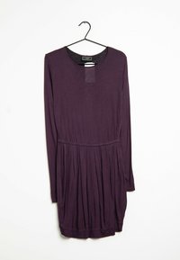 Dlouhý fialový šaty s kulatým výstřihem, skládáním v pase a měkkou texturou, visiace ze černého háčku na bílém pozadí.