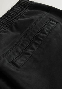 Black fabric shorts with an elastic waistband, featuring a zippered pocket on the back and smooth texture, stitched detailing.