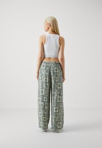 Biely rebrovaný crop top v kombinácii s voľnými, vzorovanými nohavicami s kvetinovým dizajnom v zeleno-krémových farbách. Elastický pás a široké nohavice.