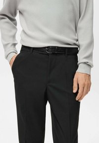Czarne spodnie garniturowe z gładkiej tkaniny i bocznymi kieszeniami, zestawione z jasnoszarym, prążkowanym, długim rękawem oraz błyszczącym czarnym paskiem.