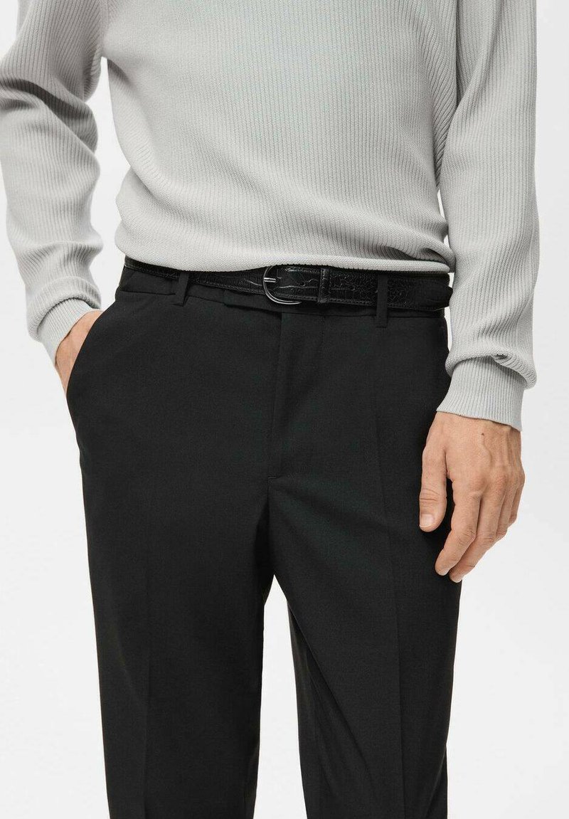 Schwarze Anzughose aus glattem Stoff mit Seitentaschen, kombiniert mit einem hellgrauen, gerippten Langarmshirt und einem glänzenden schwarzen Gürtel.