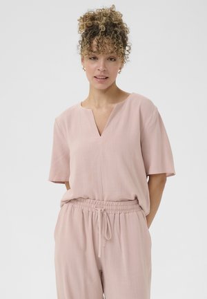 Top rosa chiaro con maniche corte, scollatura a V e vestibilità ampia. Abbinato a pantaloni in vita elastica dello stesso colore per un look coordinato. Texture morbida.