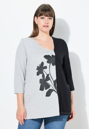 Haut gris et noir à manches trois quarts, avec un imprimé floral noir sur le côté gris et un côté noir uni. Tissu doux.