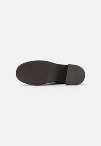 Suola di scarpa in gomma nera con motivi di grip testurizzati e tallone liscio. Il design è piano con bordi arrotondati e dettagli minimi.