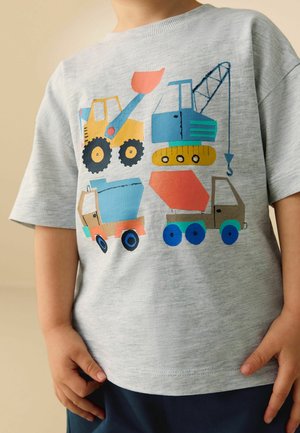 Lapsi, jolla on harmaa paita ja värikkäitä kuvia rakennusajoneuvoista, kuten puskutraktori, nosturi, betonisekoitin ja avolavakuorma-auto.