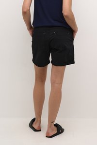 Melnas džinsas šortos ar salocītas apakšmalas, aizmugurējām kabatām un zelta aksesuāriem. Kombinēti ar tumšu augšu un melniem slaidiem sandaliem.