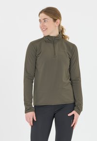 Oliivivihreä pitkähiha pullover, jossa on puolivetoketjullinen kaulus, teksturoitu kangas ja istuva muotoilu. Yhdistetty mustiin housuihin, mikä korostaa toimivuutta.