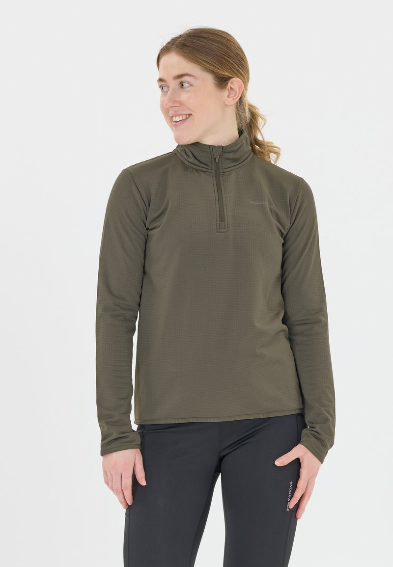 Oliivivihreä pitkähiha pullover, jossa on puolivetoketjullinen kaulus, teksturoitu kangas ja istuva muotoilu. Yhdistetty mustiin housuihin, mikä korostaa toimivuutta.