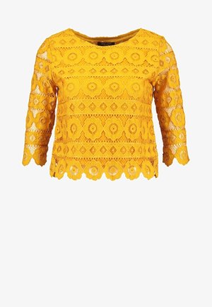 Haut en dentelle jaune avec des manches trois-quarts, orné de motifs floraux et en diamant, avec un ourlet en scallop et un col rond.