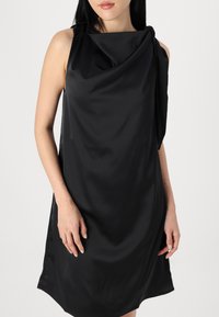 Svart ärmlös klänning i slät tyg, med en draperad halsringning och en enda axeldetalj, lätt figurnära form.