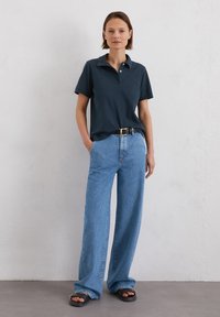 Donkerblauwe polo, lichtblauwe wijde jeans, zwarte riem en zwarte sandalen. Eenvoudig ontwerp, korte mouwen en effen kleuren.