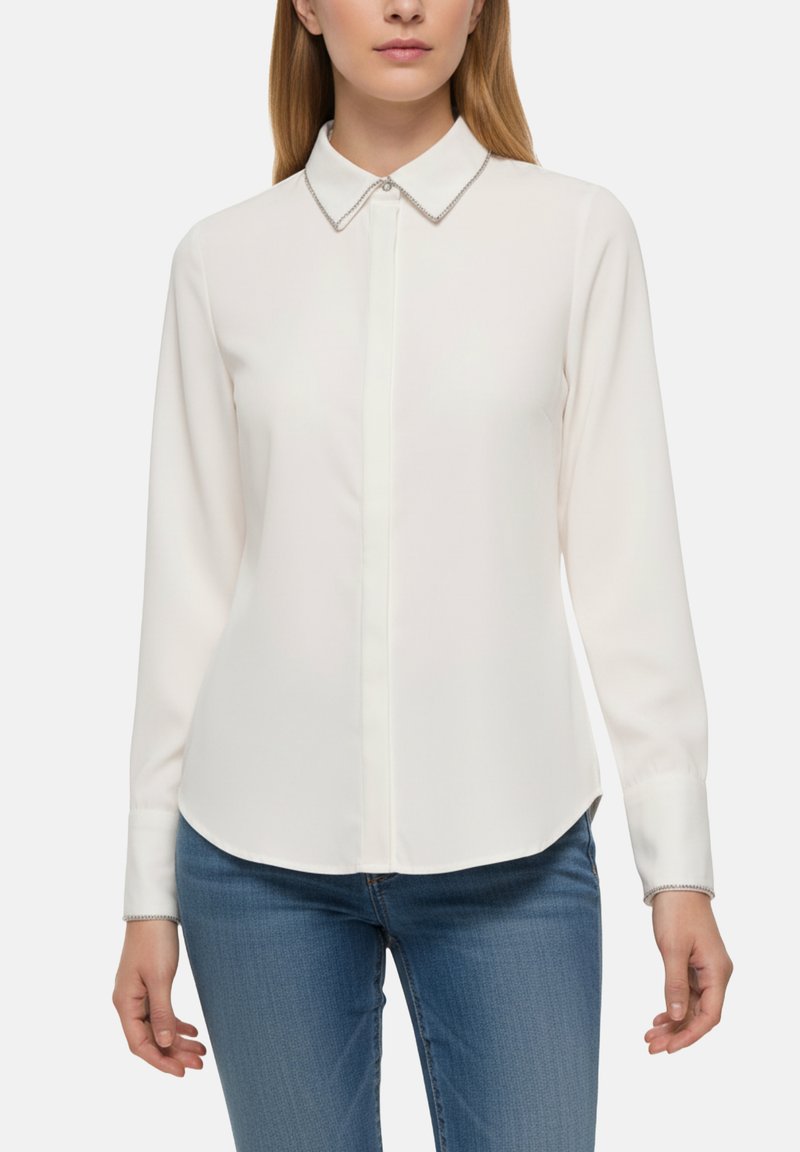 Blusa bianca a maniche lunghe con colletto a punta, caratterizzata da un dettaglio di catena decorativa sul colletto e sulla pattina dei bottoni, texture liscia.