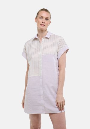 Femme à la peau claire et aux cheveux blonds portant une robe à manches courtes à boutons avec des rayures verticales mélangées dans des tons pastel.