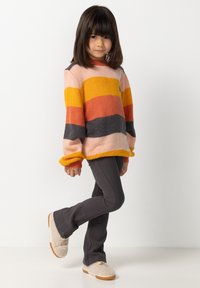 Pull rayé coloré avec des teintes de rose, orange et gris, associé à un pantalon côtelé gris foncé et des chaussures duveteuses de couleur claire.