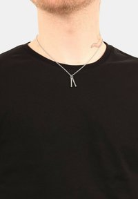 Collana in argento con due pendenti allungati dalle punte arrotondate, indossata su uno sfondo di t-shirt nera.