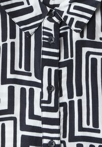 Camicia a maniche corte in bianco e nero con un motivo geometrico a labirinto, dotata di colletto a punta e bottoni neri sul frontale.