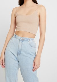 Beige ribbat crop top med tunna band, kombinerad med ljusblå högmidjade jeans. Tyget har en subtil glans.