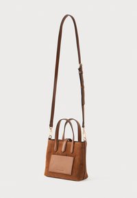 Καφέ σουέτ τσάντα χειρός με διπλούς χειρολαβές και αποσπώμενος ιμάντας ώμου. Διαθέτει μπροστινή τσέπη με πα patch τσέπη και χρυσά στοιχεία. 