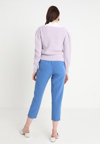 Pull côtelé violet clair avec manches bouffantes et ourlet ajusté, associé à un pantalon tailleur bleu clair et des talons ouverts en argent.