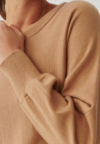 Vaaleanruskea neulottu neulepaita, leveä kaula-aukko ja pitkät hihat. Kangas on pehmeä, resorit hihansuissa ja rento istuvuus.