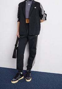 Svart blazer över en grå crop top, matchad med svarta joggare med vita ränder. Bärs med svarta sneakers och en svart axelväska.