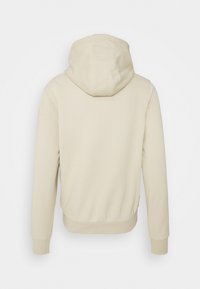 Sudadera con capucha beige de textura suave, con puños y dobladillo acanalados, que presenta un corte relajado y costuras lisas. Vista trasera.