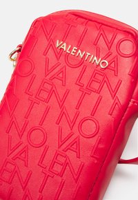 Mala transversa de couro vermelho com marcação em relevo. Os detalhes em dourado complementam a superfície texturizada. Design retangular compacto.