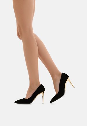 Scarpe nere in suede con tacco alto, dalla punta appuntita e tacchi sottili color oro, che mettono in mostra una texture liscia e un design minimalista.