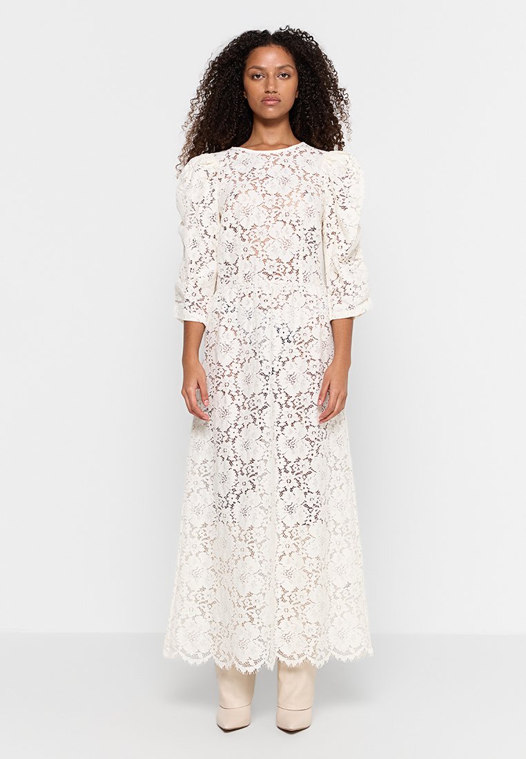 Weißes Spitzen-Maxikleid mit Puffärmeln, floralem Muster und gewelltem Saum; getragen mit nudefarbenen Knöchelstiefeln.