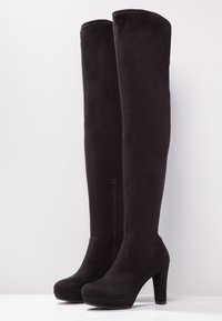 Botas negras de ante por encima de la rodilla, con cierre de cremallera en el lado, un tacón de plataforma y textura suave y mate.