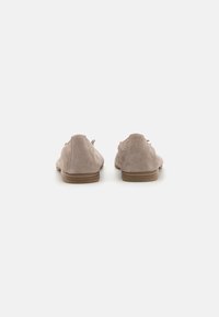 Par de zapatos de ante beige claro de tacón bajo con respaldos redondeados y suelas de madera apiladas sobre un fondo blanco liso.